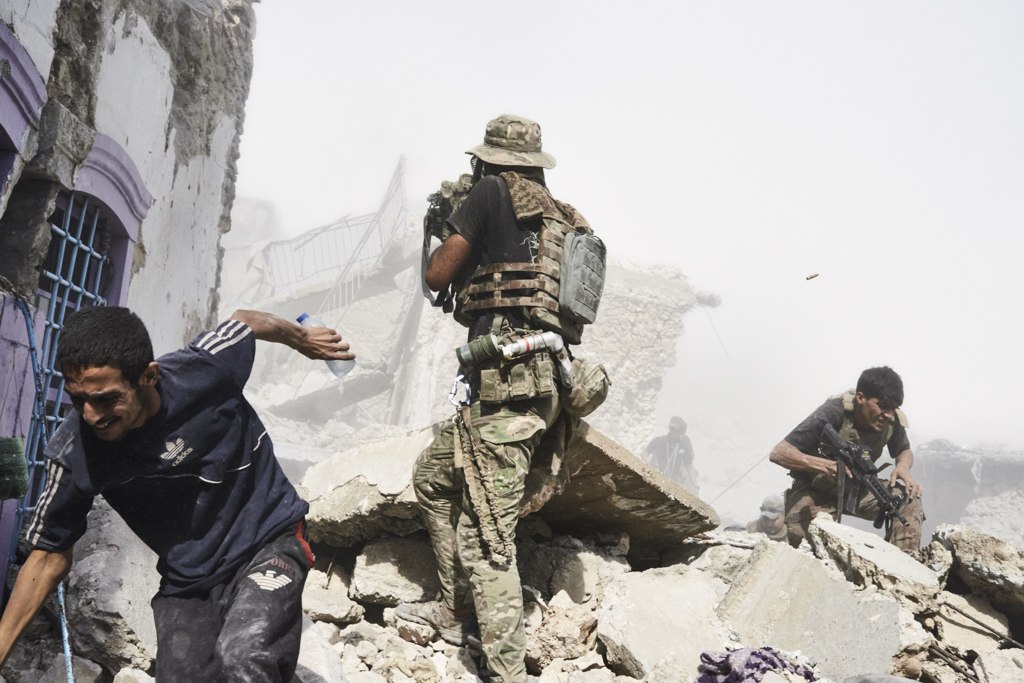 Mosul, Iraq. Luglio 2017 - Un civile fuggito da un’area sotto controllo dell’ISIS cerca rifugio, mentre soldati delle Forze Speciali irachene combattono nella Città Vecchia di Mosul.